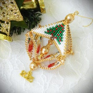 May include: A handmade Christmas bauble with a white beaded design, featuring a green and red tree pattern. The ornament has gold accents and a small charm with the year "2025". Festive holiday decoration.