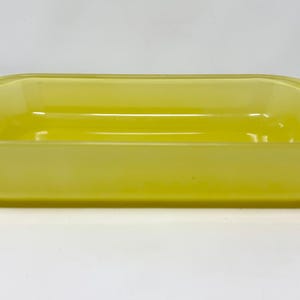 Könnte beinhalten: Eine rechteckige, gelbe Backform aus Glas. Die Form hat abgerundete Ecken und einen leicht gebogenen Rand. Das Glas hat eine durchscheinende Qualität, und die Form ist leer. Der Hintergrund ist weiß.