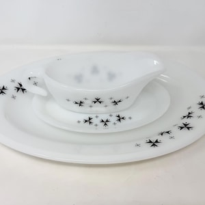May include: A white vintage dish set with a gravy boat, a small plate, and a large plate. Each piece is decorated with a black starburst pattern. The set is arranged on a white surface.