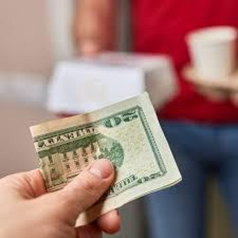 May include: A hand holding a twenty-dollar bill, featuring Andrew Jackson's portrait. The bill is creased, with green and tan hues. In the background, a person is holding food and drinks.