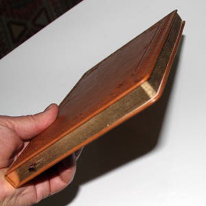 May include: A brown leather-bound journal with gold edging. The journal is closed and held in a hand.