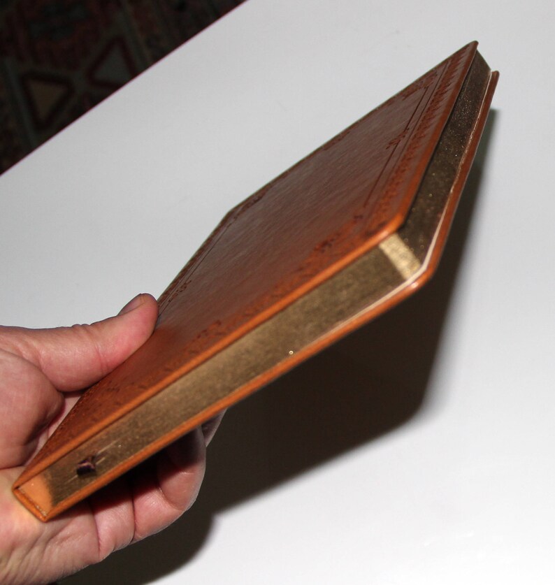 May include: A brown leather-bound journal with gold edging. The journal is closed and held in a hand.
