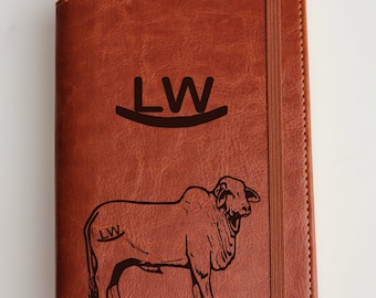 May include: A brown leather journal with a black engraved design of a cow and the initials "LW".