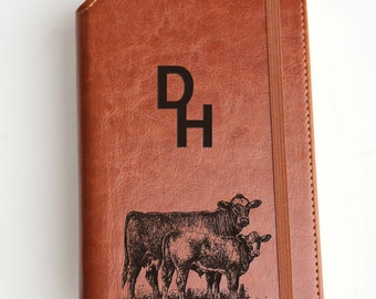 May include: A brown leather journal with a black engraved design of two cows and the initials "DH".