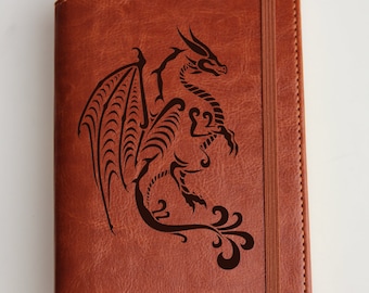 May include: A brown leather journal with a black dragon design and the word "DRAGON" engraved on the front.