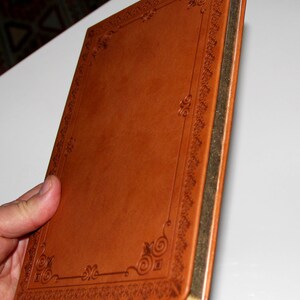 May include: A brown leather-bound journal with a gold-colored edge and an intricate embossed design around the cover.