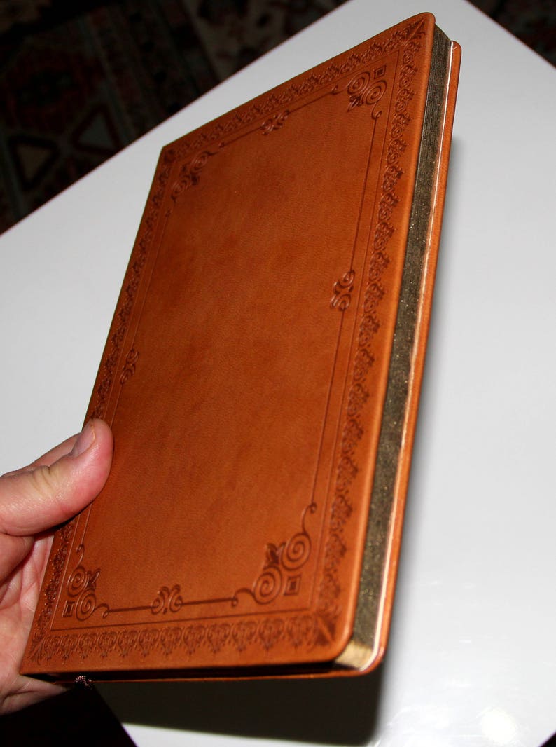 May include: A brown leather-bound journal with a gold-colored edge and an intricate embossed design around the cover.