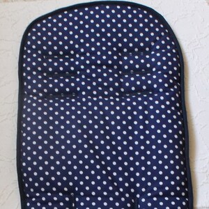 Op de afbeelding: Een donkerblauwe kinderwagen-zittingbekleding met een wit stippenpatroon. De bekleding heeft een gevoerde hoofdsteun en twee banden om hem aan de kinderwagen te bevestigen.