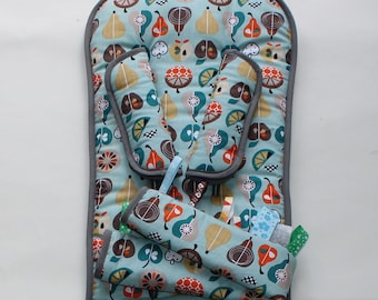 May include: A baby stroller insert with a light blue background and a pattern of colorful fruit illustrations. The insert has a gray border and includes head and shoulder supports, along with a small toy attachment. The insert measures approximately 28 inches long.