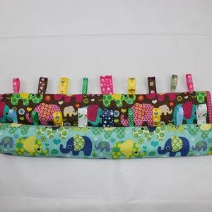May include: Two fabric baby teethers with colourful elephant patterns and ribbons. The top teether is brown with pink, yellow, and green ribbons. The bottom teether is blue with green and yellow ribbons.
