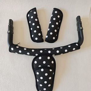 May include: Black and white polka dot stroller handlebar covers. The set includes two armrest covers, a handlebar cover, and a crotch strap cover.