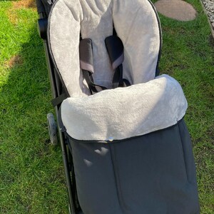 Könnte beinhalten: Ein schwarzer Kinderwagen mit einem grauen Fleece-Futter. Der Kinderwagen hat einen Fünf-Punkt-Gurt und einen großen Ablagekorb.