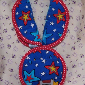 May include: A set of blue fabric harness covers featuring a pattern of red, yellow, and light blue stars with white accents. The covers have a rounded shape with red and white polka dot trim along the edges and include a central buckle component.