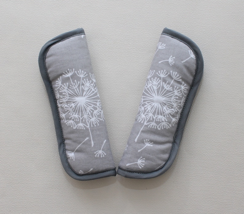 May include: A pair of grey fabric shoulder pads with a white dandelion print. The shoulder pads are lined with grey fabric and have a soft, padded feel.