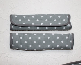 May include: Two grey fabric items with white polka dots. One is rectangular with a rounded flap, the other is a long rectangle. Both have a dark grey trim. The items appear to be handmade.