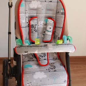 Könnte beinhalten: Ein grauer und weißer Kinderwagen-Einsatz mit Zebra-, Bären- und Giraffenmuster. Der Einsatz hat einen roten Rand und eine türkisfarbene Akzentfarbe. Der Einsatz ist für einen Kinderwagen konzipiert.