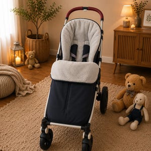 Op de afbeelding: Een marineblauwe en zilveren kinderwagen met een zacht, lichtgrijs interieur. De kinderwagen heeft een bordeauxrode handgreep en zwarte wielen. Een teddybeer en een knuffelkonijn liggen in de buurt op het tapijt.