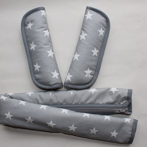 May include: A set of grey and white stroller straps with a zipper. The straps have a white star pattern.