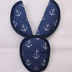 May include: A navy blue fabric accessory featuring a repeating white anchor pattern. The item consists of a rounded base section and two elongated, pointed upright extensions, all finished with a dark navy blue piped edge trim throughout.