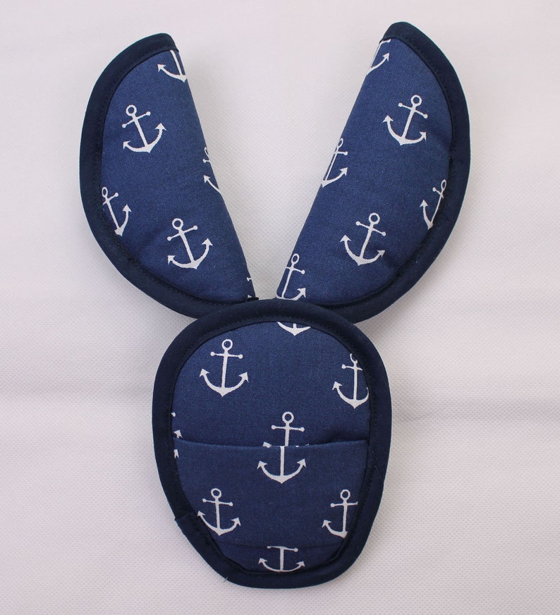May include: A navy blue fabric accessory featuring a repeating white anchor pattern. The item consists of a rounded base section and two elongated, pointed upright extensions, all finished with a dark navy blue piped edge trim throughout.