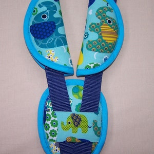 May include: A set of three padded strap covers for a harness system, featuring a light blue fabric with a colorful elephant and floral pattern. The covers are trimmed in bright blue and are attached to dark blue nylon webbing straps.