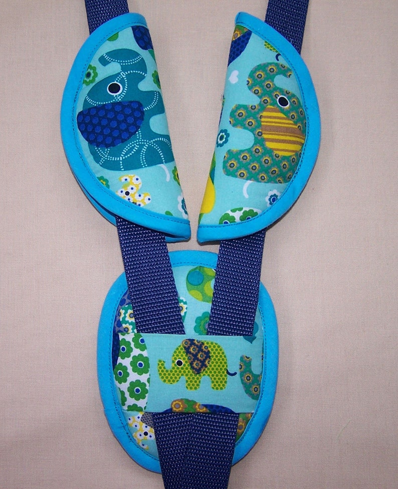 May include: A set of three padded strap covers for a harness system, featuring a light blue fabric with a colorful elephant and floral pattern. The covers are trimmed in bright blue and are attached to dark blue nylon webbing straps.