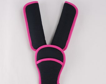 May include: Black safety harness with pink trim. The harness has two straps and a chest piece.