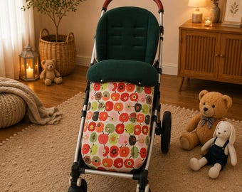 May include: A modern stroller with a dark green seat and a colorful apple-patterned fabric basket. The stroller has a brown handle and a silver frame. The wheels are black. The stroller is on a beige rug.