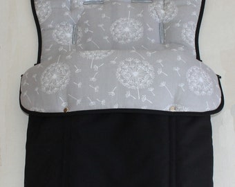 May include: A gray and black stroller insert with a dandelion pattern. The upper portion features a light gray fabric with white dandelion designs and a black trim. The lower section is solid black. Includes slots for straps.