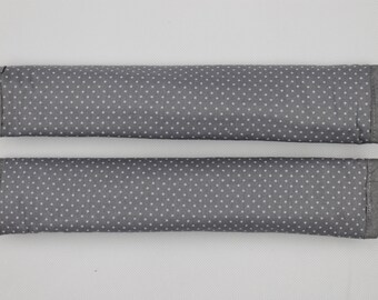 May include: Two rectangular fabric covers in a dark grey colour featuring a repeating pattern of small white polka dots. Each cover has finished edges and a consistent cylindrical shape, designed to wrap around handles or bars for added comfort.