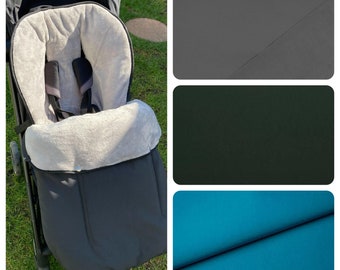 May include: A black stroller footmuff with a gray fleece lining. The footmuff is shown in a stroller with a gray, green, and blue fabric swatches in the background.