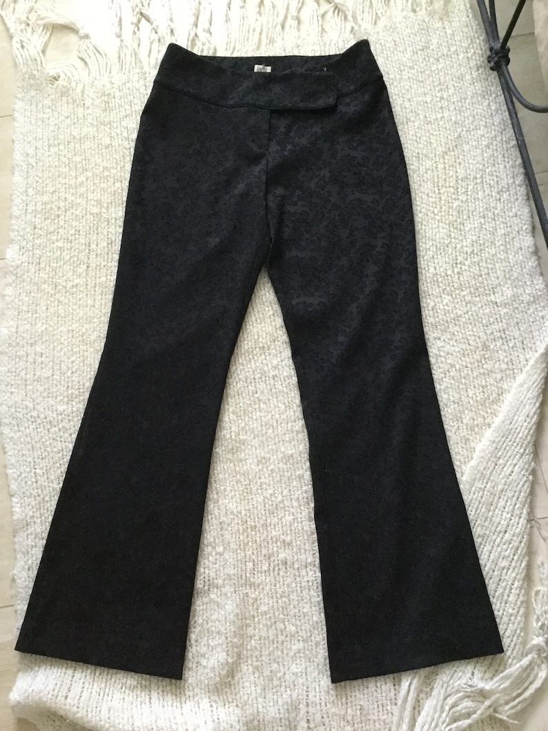 Puede incluir: Pantal&oacute;n negro acampanado con un sutil estampado floral. El pantal&oacute;n tiene una cintura con cierre de bot&oacute;n y cremallera.