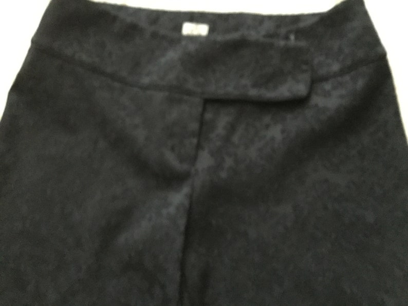 Puede incluir: Pantal&oacute;n negro de tela texturizada ligeramente brillante. El pantal&oacute;n tiene una cintura con bot&oacute;n y cierre de cremallera.