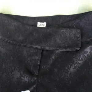 Puede incluir: Pantal&oacute;n negro con estampado floral y una etiqueta que dice "Cache" en la cintura.