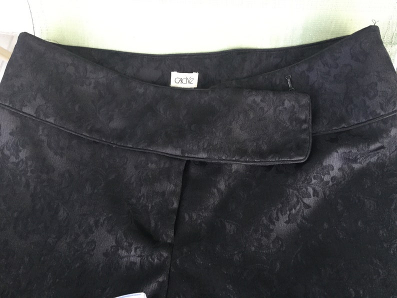 Puede incluir: Pantal&oacute;n negro con estampado floral y una etiqueta que dice "Cache" en la cintura.