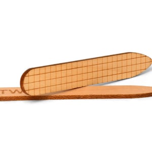 May include: Two wooden leather working tools. One tool is a flat, rectangular shape with a grid pattern. The other tool is a rounded, oval shape with the word "TW" engraved on it.