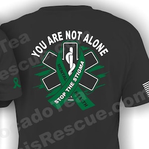 May include: Black t-shirt with a green star of life graphic and the text "You Are Not Alone" and "Stop The Stigma Mental Health". The shirt also features a small patch with the text "Titchen County EMS".