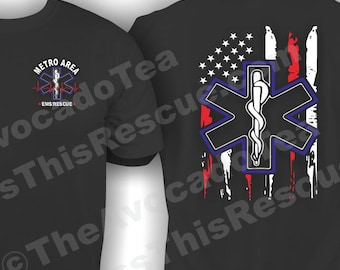 May include: Black t-shirt with a distressed American flag design featuring a blue medical star of life symbol. The front of the shirt has the text "METRO AREA EMS RESCUE" in white.
