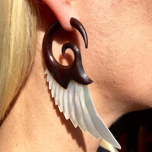 May include: A pair of wooden ear gauges with a spiral design and a white mother-of-pearl wing design.