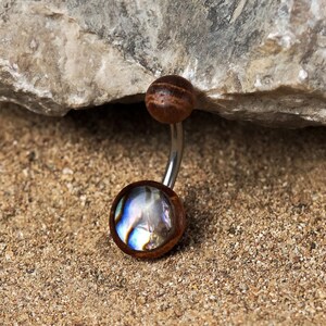May include: A silver belly button ring with a brown wooden top and a blue and iridescent abalone shell bottom.