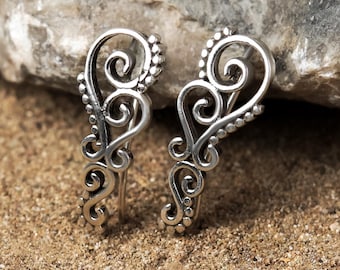 May include: A pair of silver earrings with a delicate, intricate design. The earrings are made of a filigree pattern with small beads along the edges.