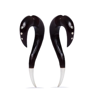 May include: A pair of dark brown, curved earrings with a white tip. The earrings have a teardrop shape with small silver accents. The background is plain white.