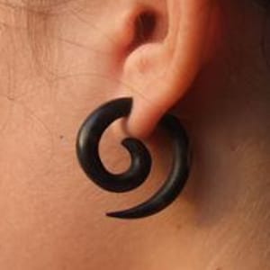 May include: A pair of black spiral wood ear gauges. The gauges are made of wood and have a spiral design. They are worn in the earlobes.