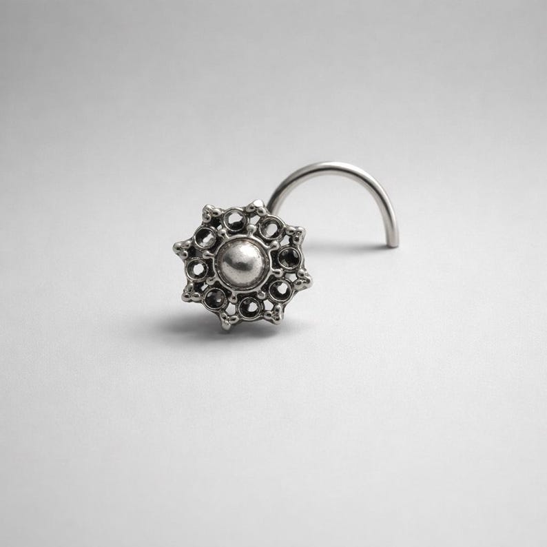 Pode incluir: Um piercing de nariz prateado com um design decorativo em forma de raio de sol. O piercing apresenta uma conta central redonda rodeada por pequenos detalhes circulares. A haste curva &eacute; vis&iacute;vel, projetada para perfura&ccedil;&atilde;o.
