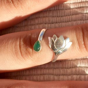 Op de afbeelding: Een zilveren ring met een groene steen en een lotusbloem ontwerp.