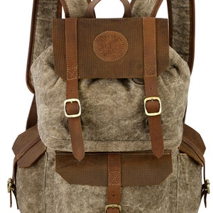 Peut inclure: Un sac à dos en toile marron avec des accents en cuir et des boucles. Le sac à dos a un grand compartiment principal et une petite poche avant. Le sac à dos a un patch en cuir marron avec le texte "Old Fashioned Buddy Original" dessus.