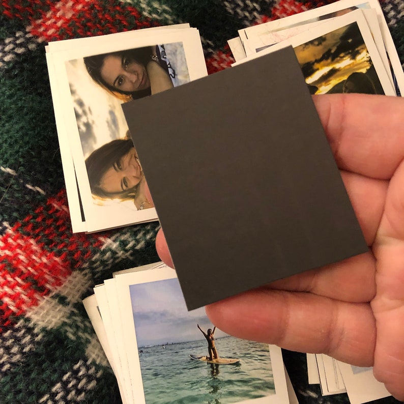 May include: A dark gray square magnet. The magnet is being held in a hand.