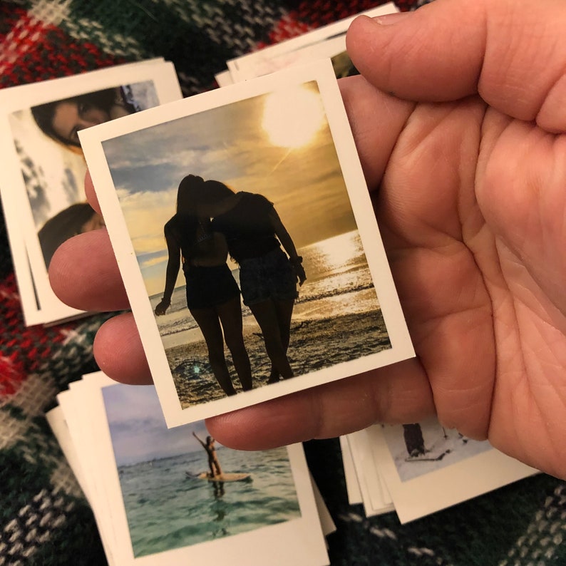 May include: Two people silhouetted against a sunset on a beach. The photo is printed on a white background with a white border.