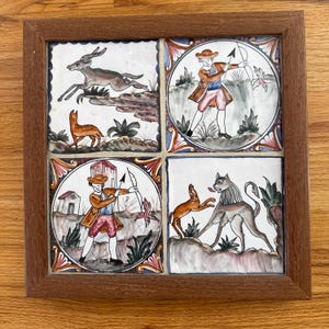 May include: A framed tile set with four different scenes. The top left tile shows a brown deer running through a green forest. The top right tile shows a man in a red and blue outfit holding a bow and arrow. The bottom left tile shows a man in a red and blue outfit holding a bow and arrow. The bottom right tile shows a brown dog running through a green forest.