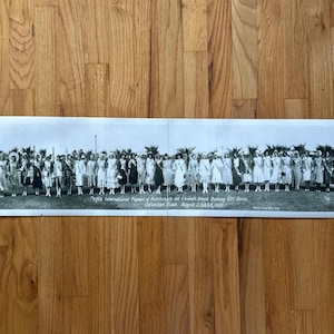 May include: A vintage black and white photograph showing a group of women in dresses and hats. The text at the bottom reads "Fifth International Pageant of Pulchritude and Eleventh Annual Bathing Girl Revue Galveston Texas, August 2,3,4,5,6, 1930."